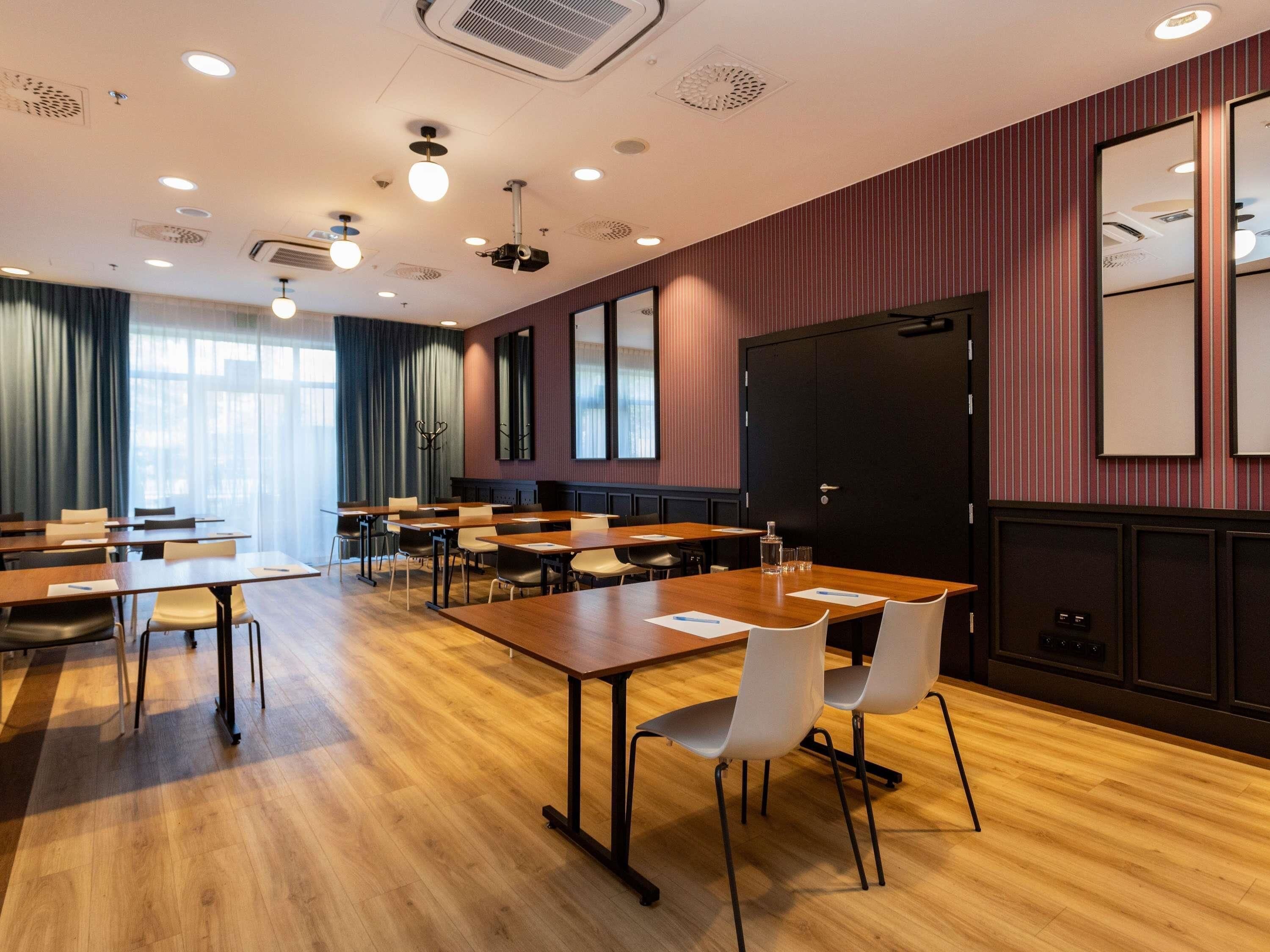 Un salón de conferencias con varias mesas y sillas, una pantalla para proyector y una puerta negra grande.