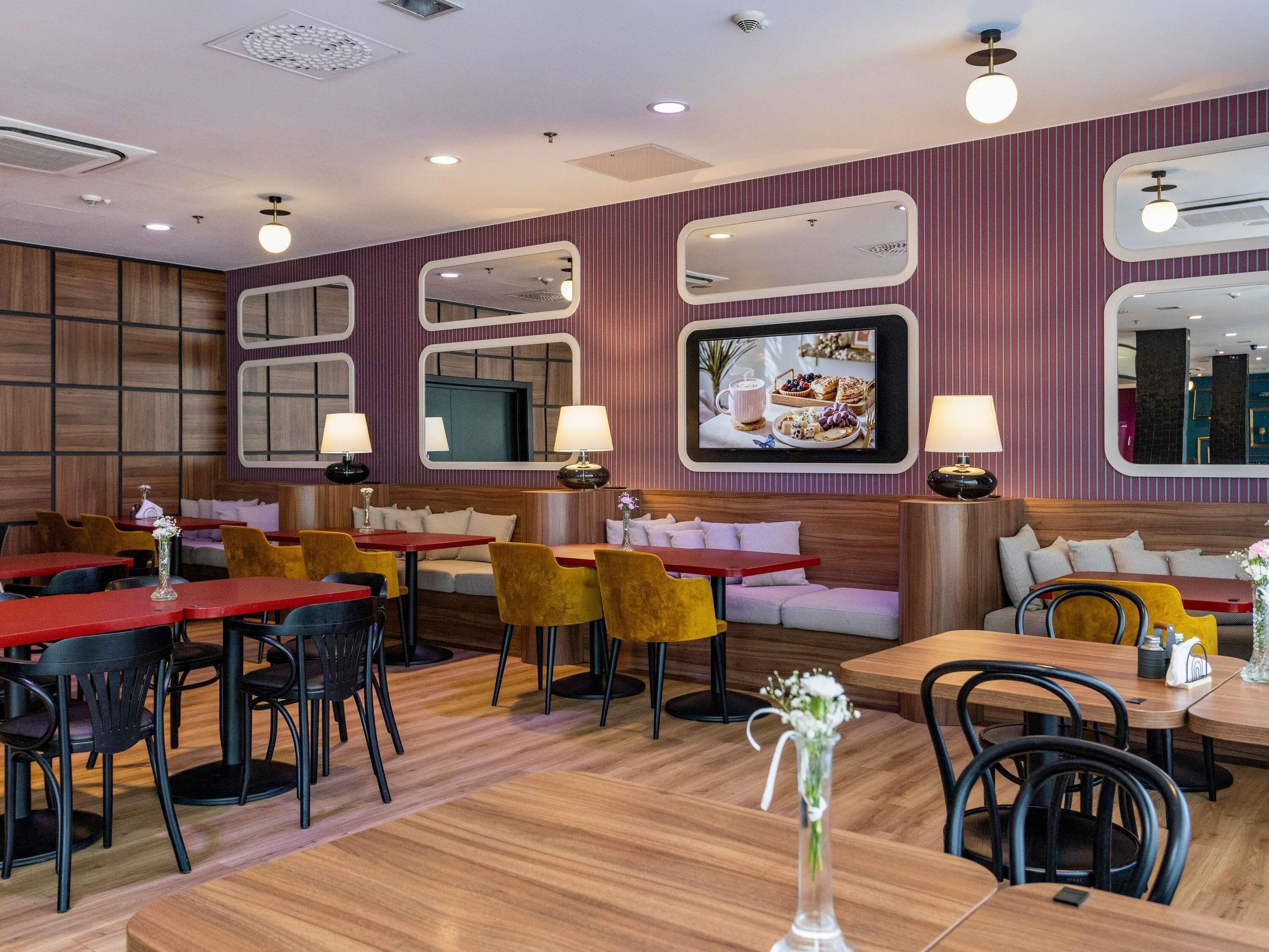 A restaurant interior with wooden flooring, red and yellow tables, and black chairs.