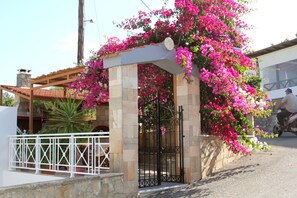 Ein überdachter Außenbereich mit Steinmauer und Metallgitter, umgeben von blühendem Rosa-Bougainvillea.