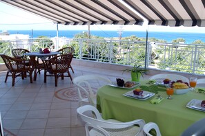 Una terraza con una mesa preparada para el desayuno, con vista a un paisaje marino.