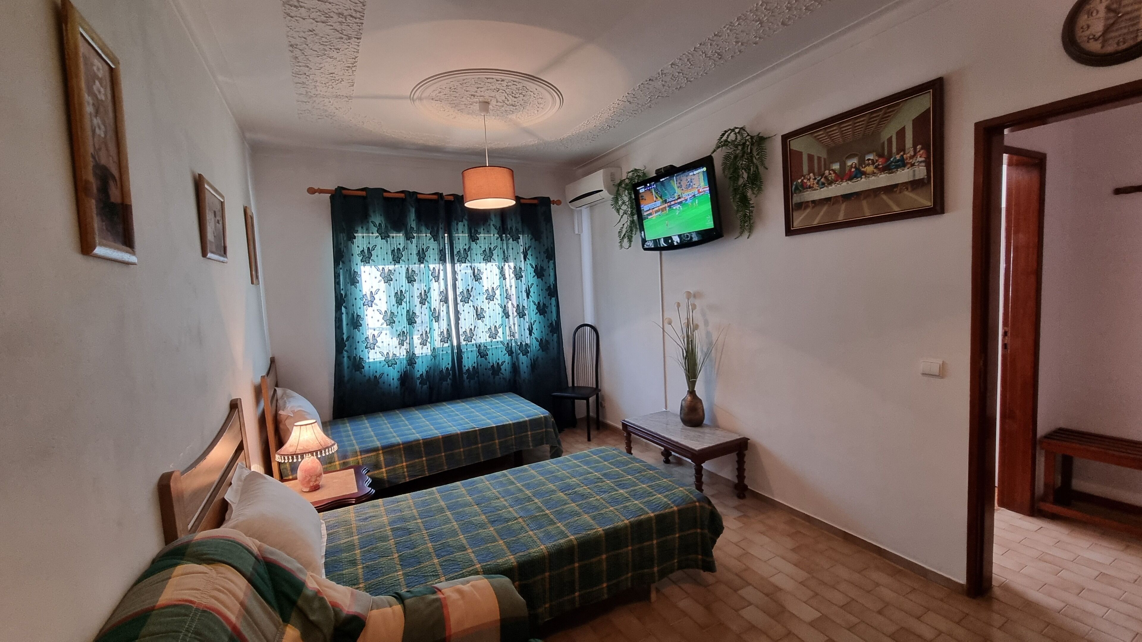 Una habitación con dos camas, televisión, un reloj y un cuadro en la pared.