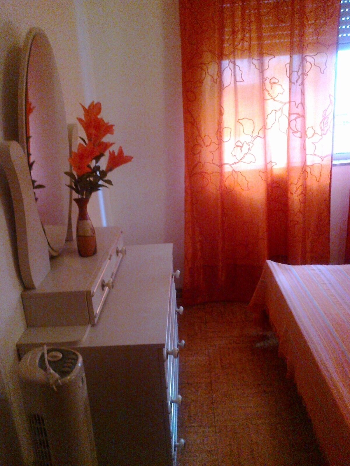 Une chambre à coucher avec un lit, une commode, un miroir et une fenêtre ornée de rideaux orange.