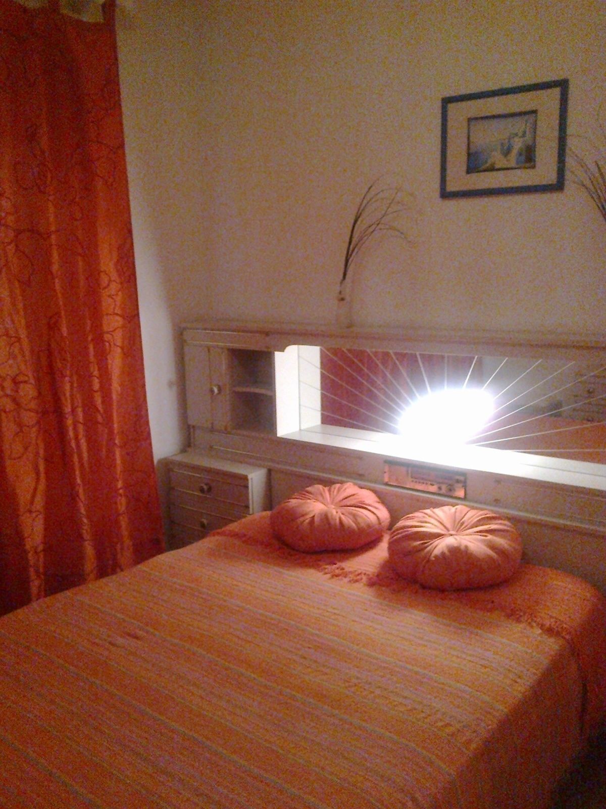 Un dormitorio con cama, dos almohadas, cómoda, espejo y ventana.