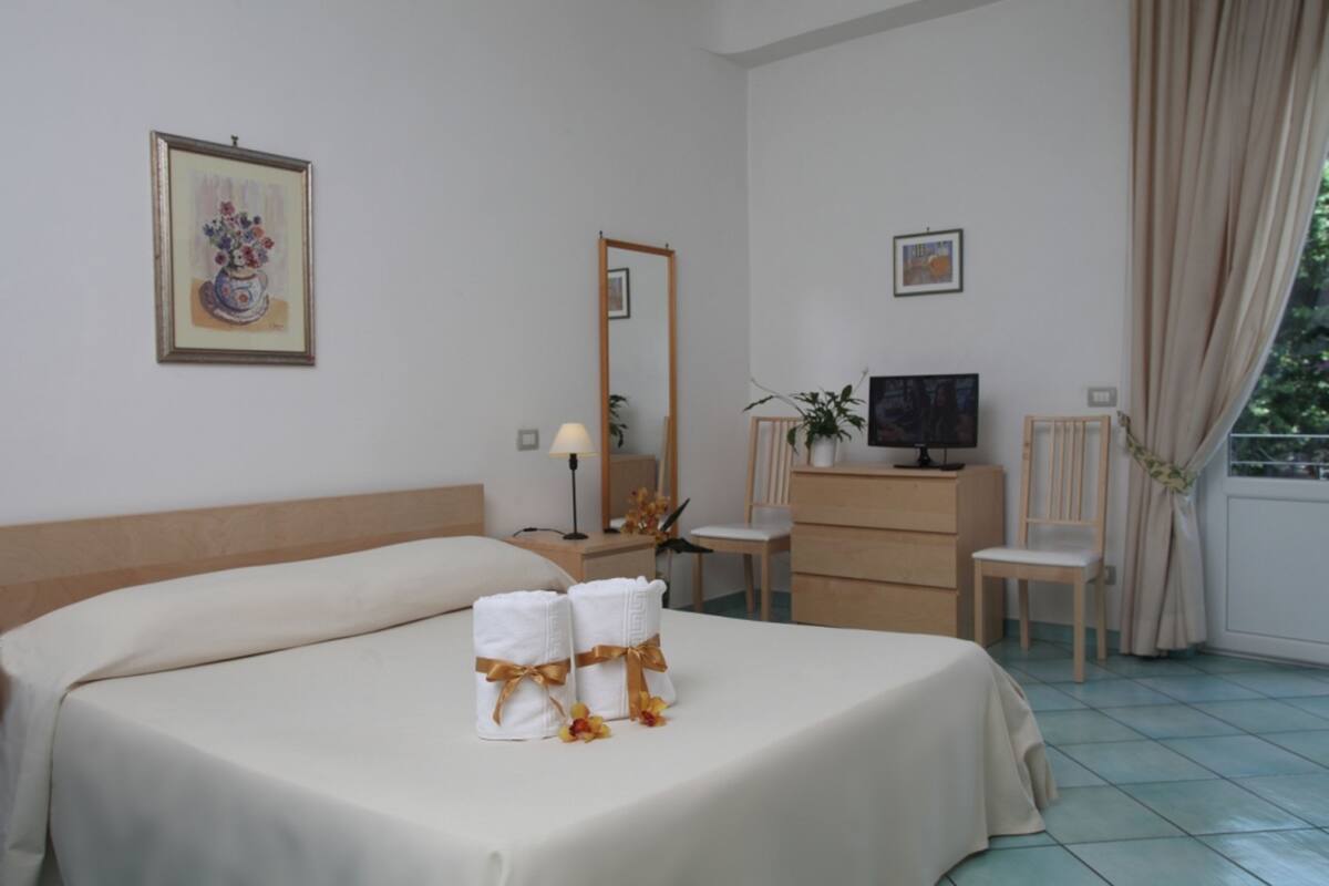 Une chambre d’hôtel comprenant un lit, deux tables de chevet, une télévision, un miroir, un bureau et une chaise.