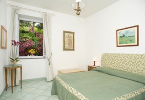 Una camera da letto con un letto, una finestra con tende, un comodino con una lampada e un quadro appeso al muro.