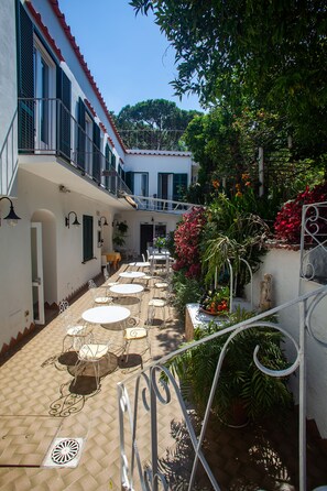 Un patio esterno con tavoli e sedie, circondato da piante e fiori in vaso.