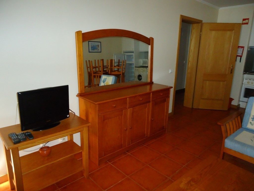 Un salon avec un meuble en bois, un téléviseur posé sur un meuble, et une porte donnant sur une autre pièce.