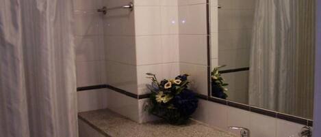 A bathroom with a white sink, a mirror, a shower curtain, and a small flower arrangement on the countertop.