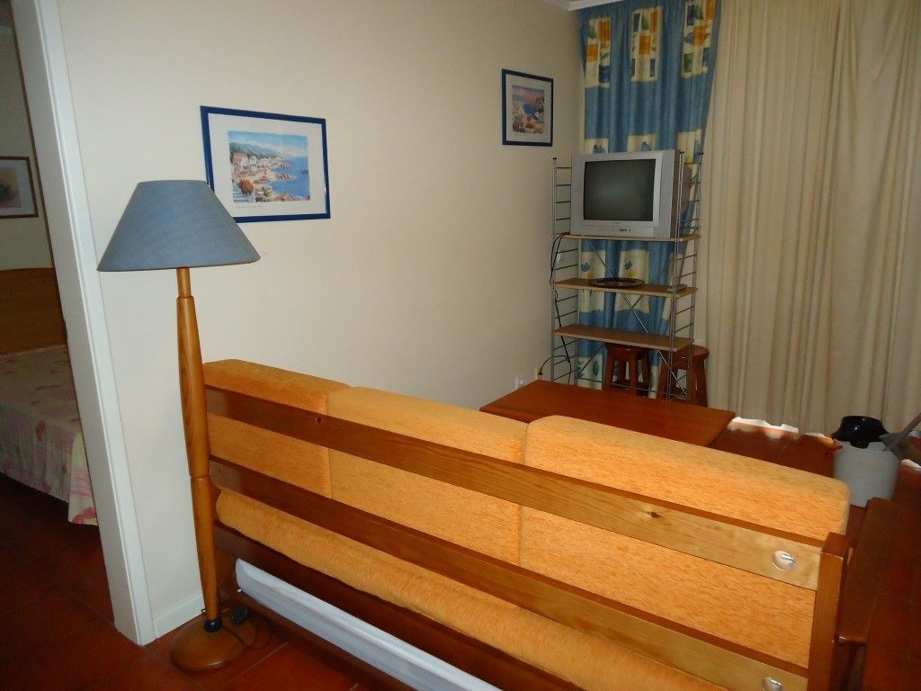 A small room with a wooden bed, a lamp, a television on a shelf, and two framed pictures on the wall.