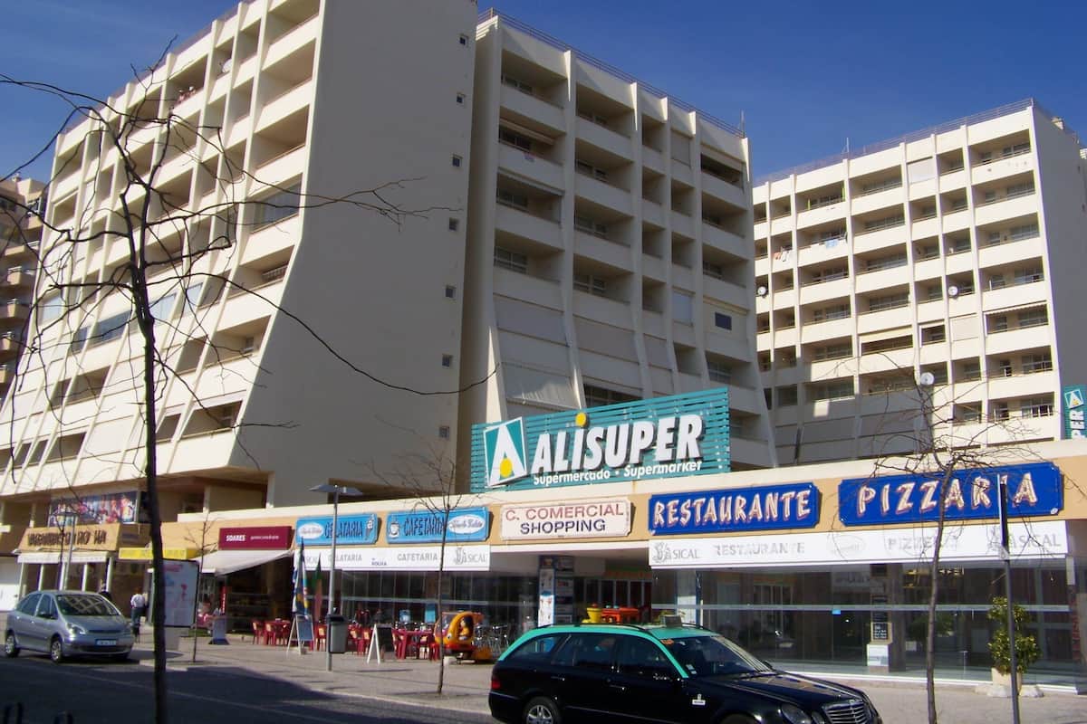Ein mehrstöckiges Geschäftsgebäude mit verschiedenen Geschäften, darunter ein Supermarkt, ein Restaurant und eine Pizzeria.