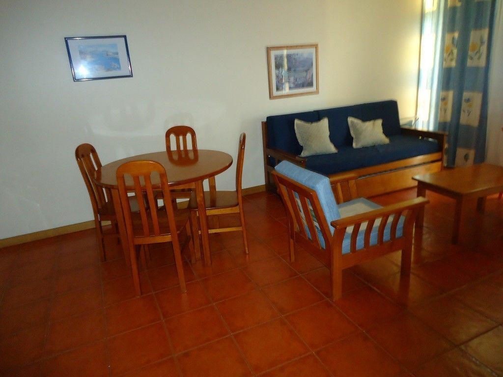 Een woonkamer met een bank, twee stoelen, een kleine tafel en twee ingelijste foto's aan de muur.