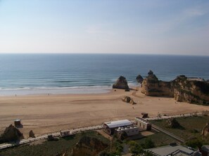 Una playa costera con formaciones rocosas, una playa de arena y una plataforma de observación con un edificio.