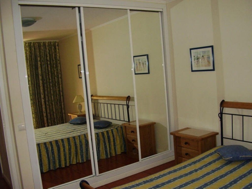 Une chambre avec une porte coulissante, un lit avec une literie à rayures, une table de chevet et une commode, ainsi que deux tableaux encadrés accrochés au mur.