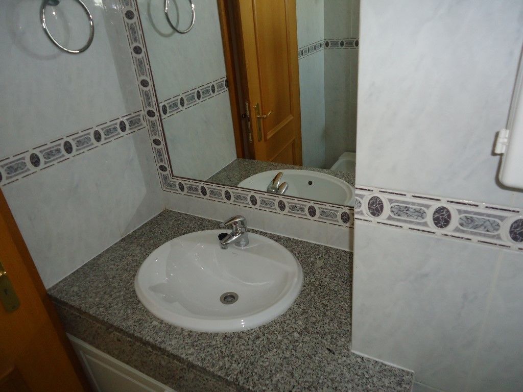 A bathroom with a white sink, granite countertop, and a mirror with decorative tiles.
