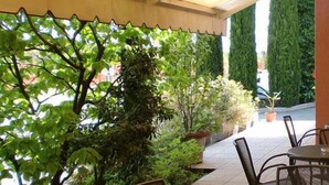 An outdoor patio area with a table and chairs, surrounded by greenery and tall plants. - Hotel Rometta (Cittadella)