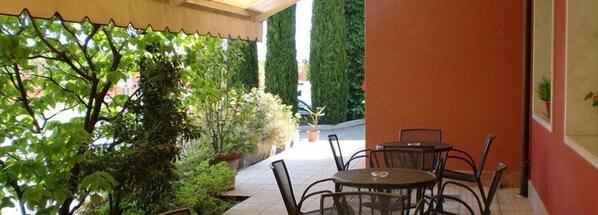 Un espace extérieur aménagé en patio, avec une table et des chaises, entouré de verdure et de grandes plantes.