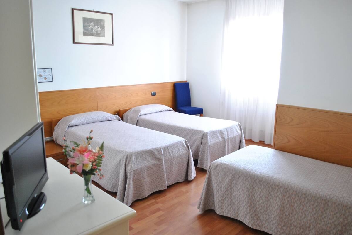 A hotel room with two single beds, a desk with a computer, and a chair.