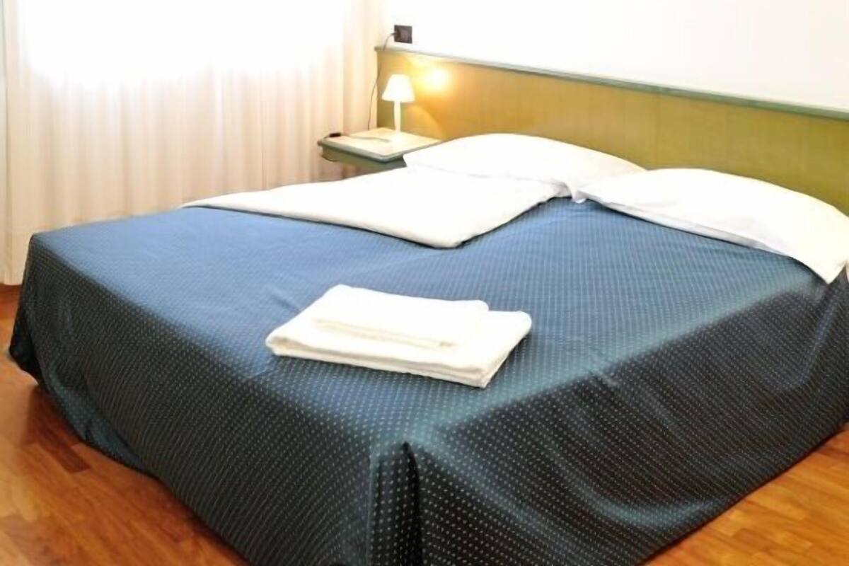 A hotel room with a bed, a nightstand, a lamp, and a cityscape painting on the wall.