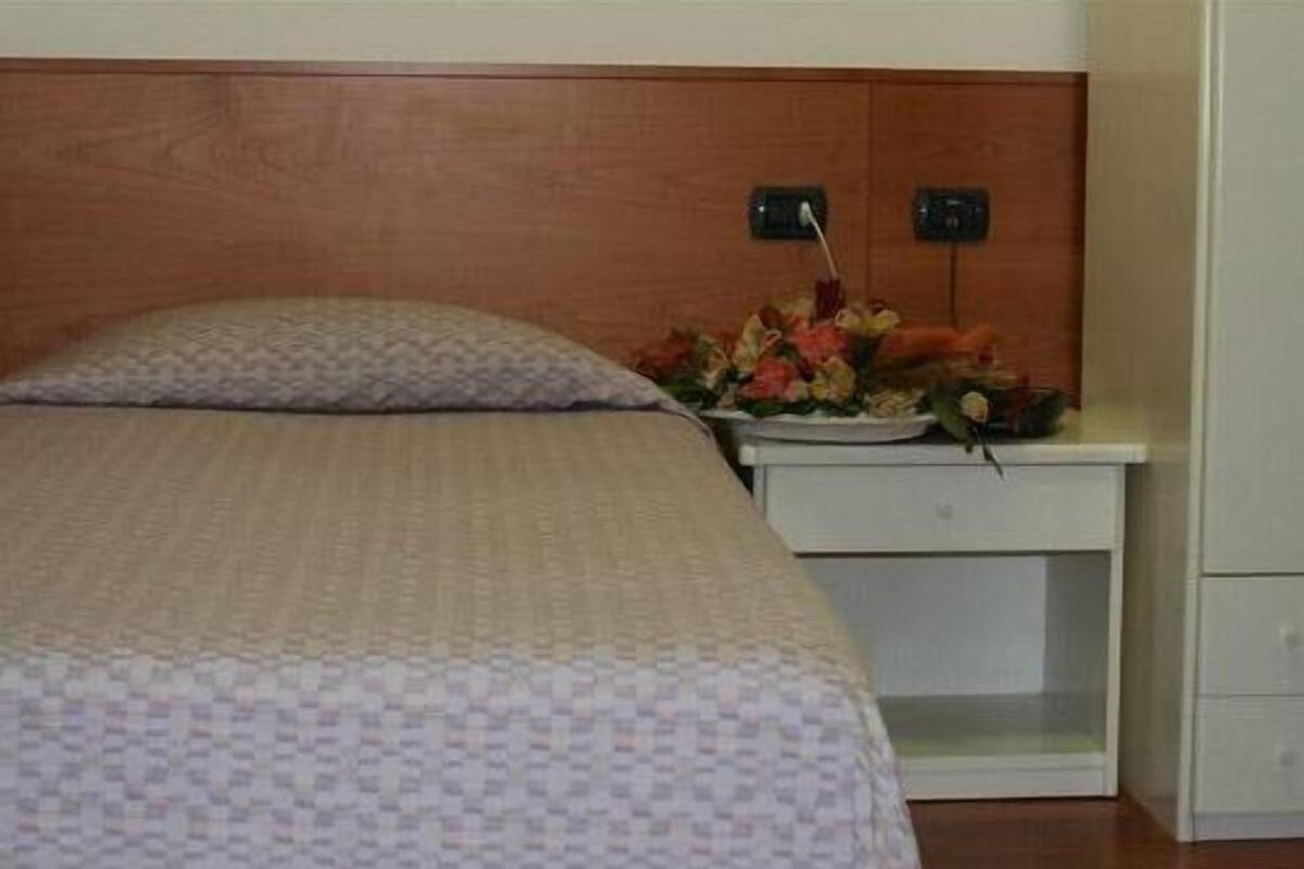 A hotel room with a bed, a nightstand with a floral arrangement, and a wooden headboard.