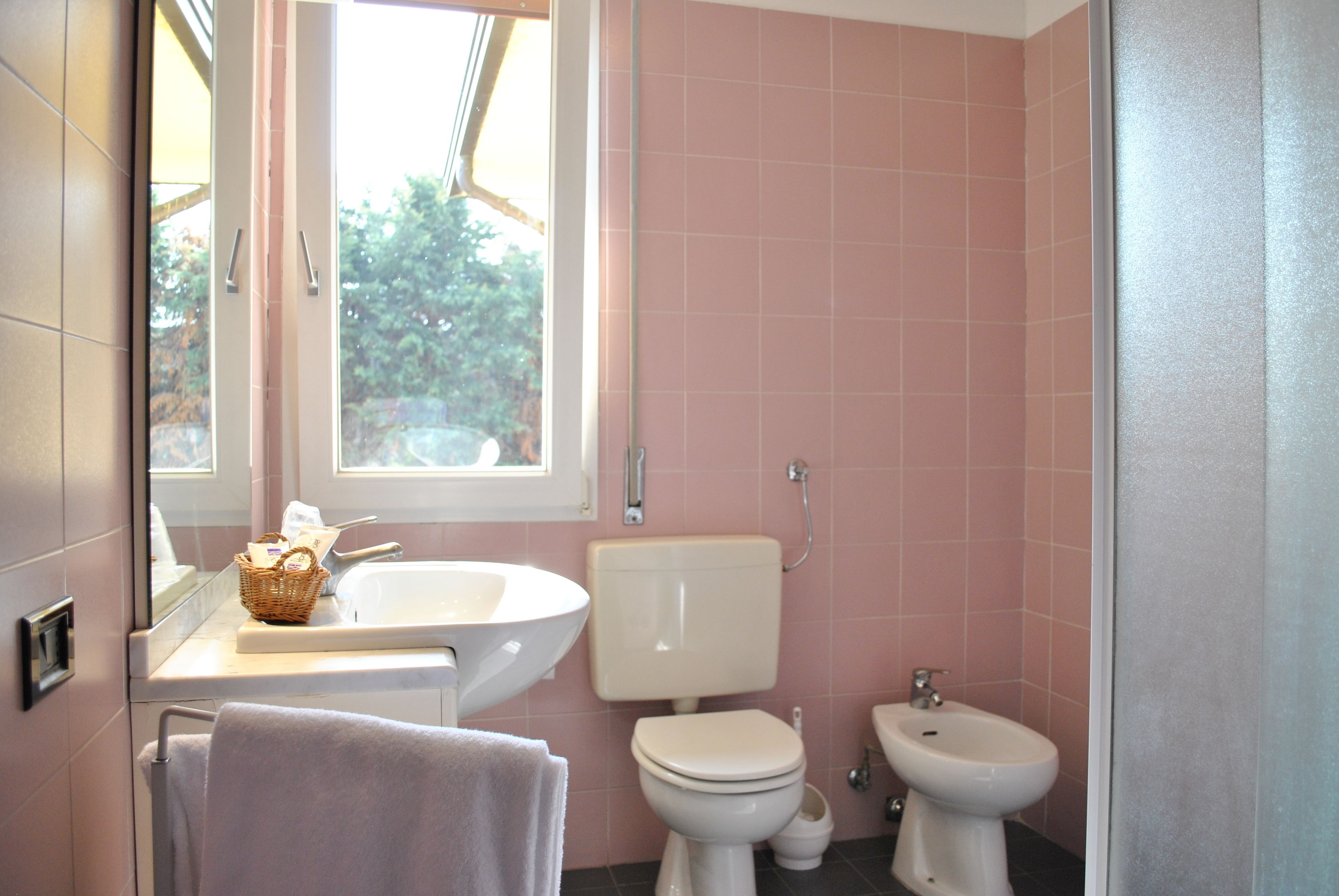 A bathroom with a sink, toilet, bidet, and a window.