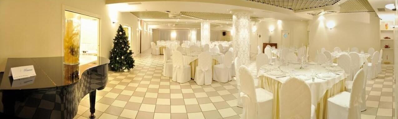 A banquet hall with round tables and white chairs, a piano, and a Christmas tree.