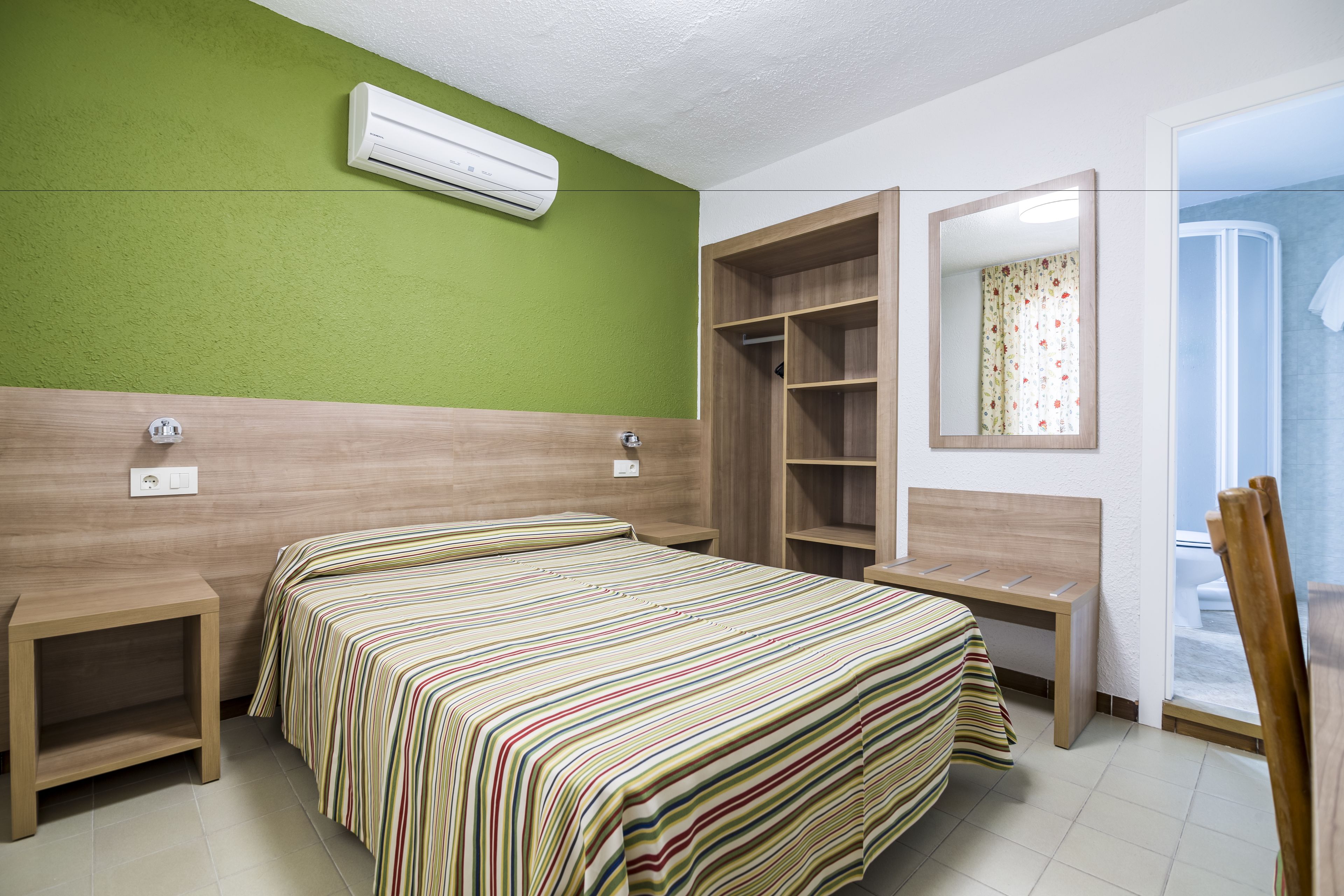 Una habitación de hotel con cama, mesitas de noche, armario y aire acondicionado en la pared.