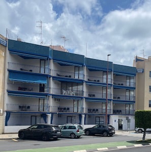 A multi-story hotel with balconies, a parking area with several cars, and a clear sky. - Hotel Blasón Junior (Peniscola)