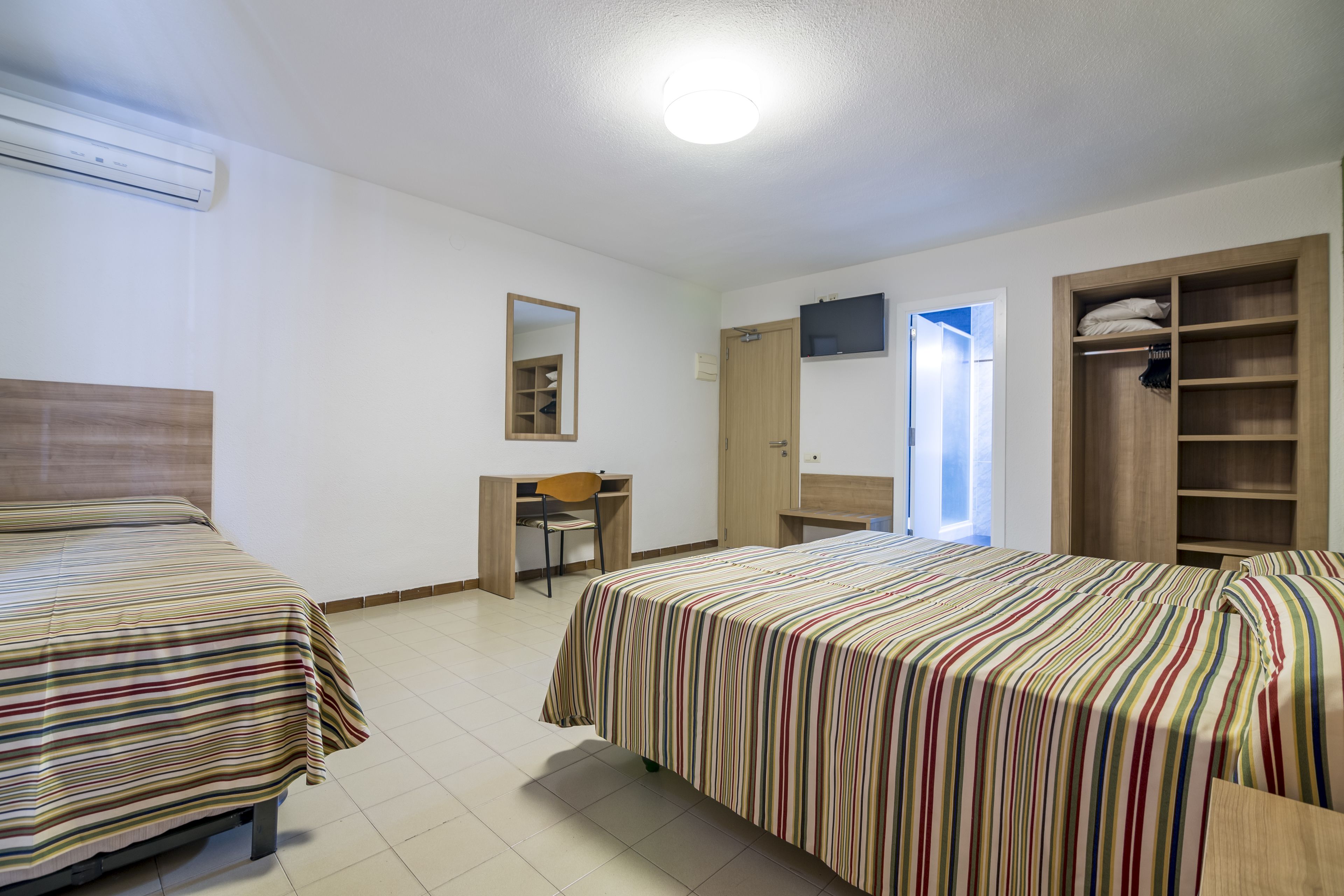 A hotel room with two beds, a desk, a chair, a TV, and a wardrobe.