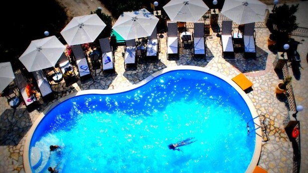 Ein Pool mit Liegestühlen und Sonnenschirmen, umgeben von einer terrasse mit Steinplatten.