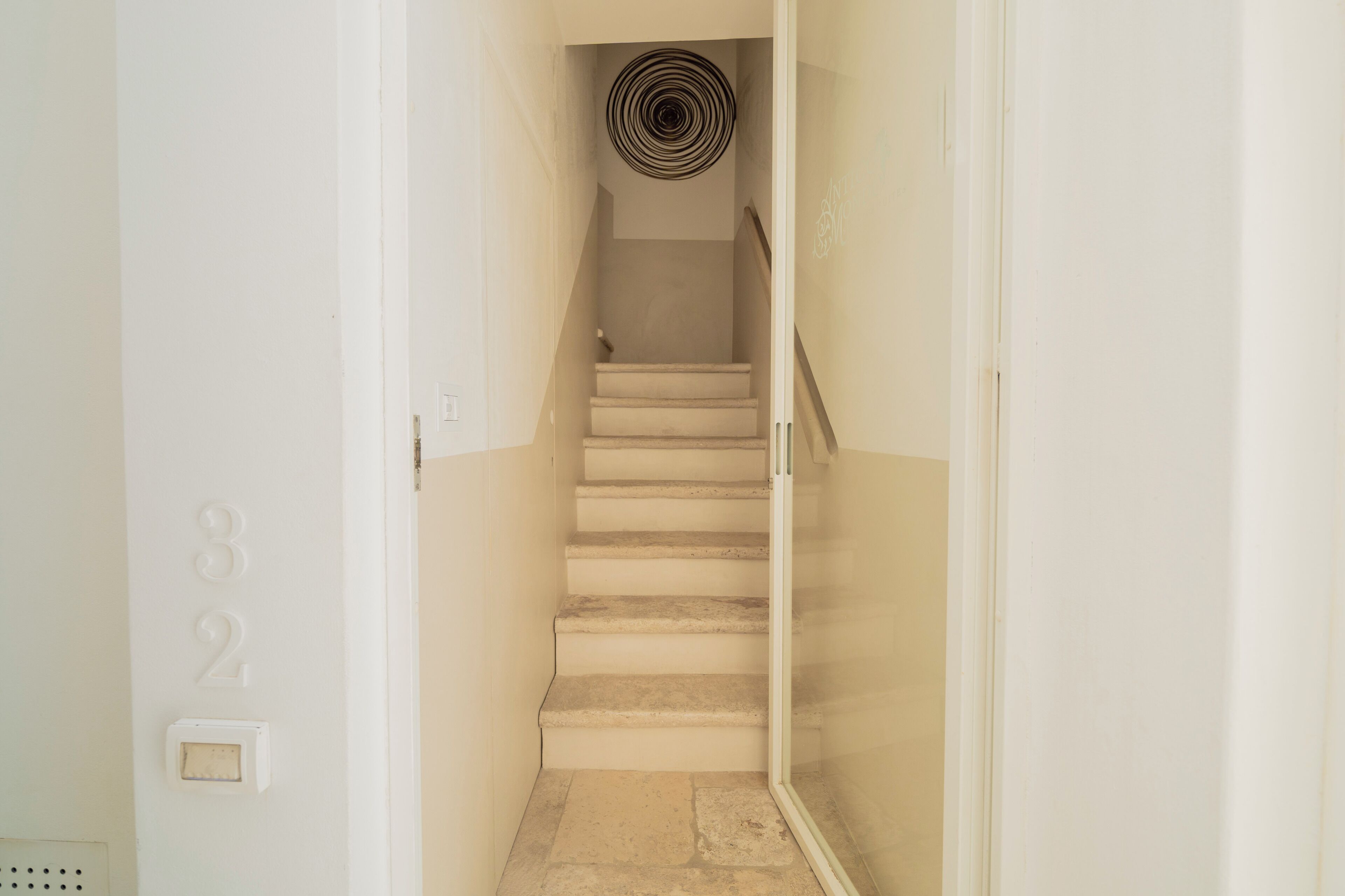 A staircase with a glass railing, a ceiling light fixture, and a door with the number 32 on the wall.