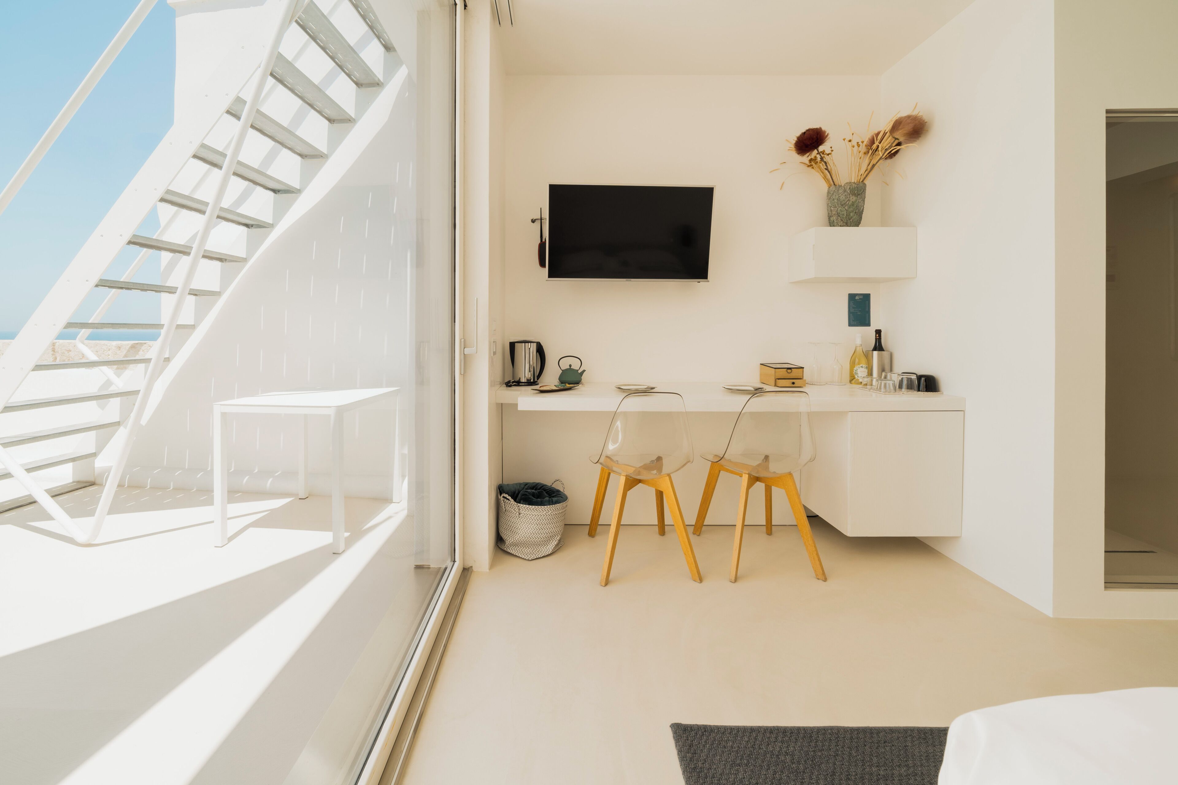A modern hotel room with a staircase, a desk with a flat-screen TV, a small seating area, and a view of the outdoors.