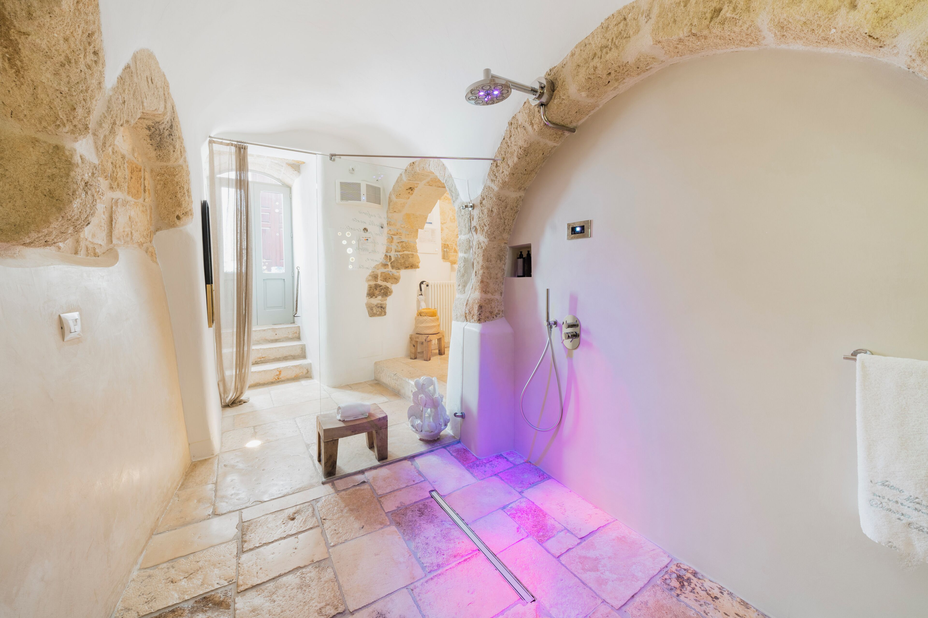 Un baño con paredes de piedra, una ducha, un taburete pequeño y un perchero para toallas.