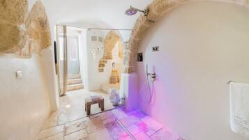 Un baño con paredes de piedra, una ducha, un taburete pequeño y un perchero para toallas.