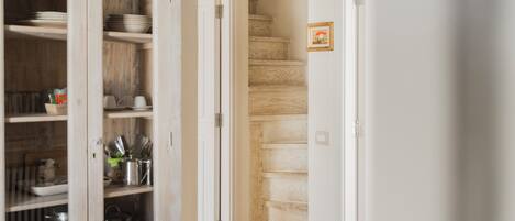 Un pasillo con una escalera de madera, un armario con utensilios de cocina y un cuadro en la pared.