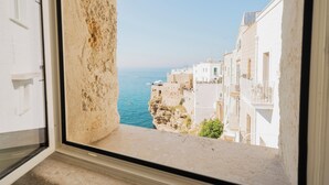Vista costera desde una ventana con vista a un acantilado, edificios, cielo despejado y el mar.