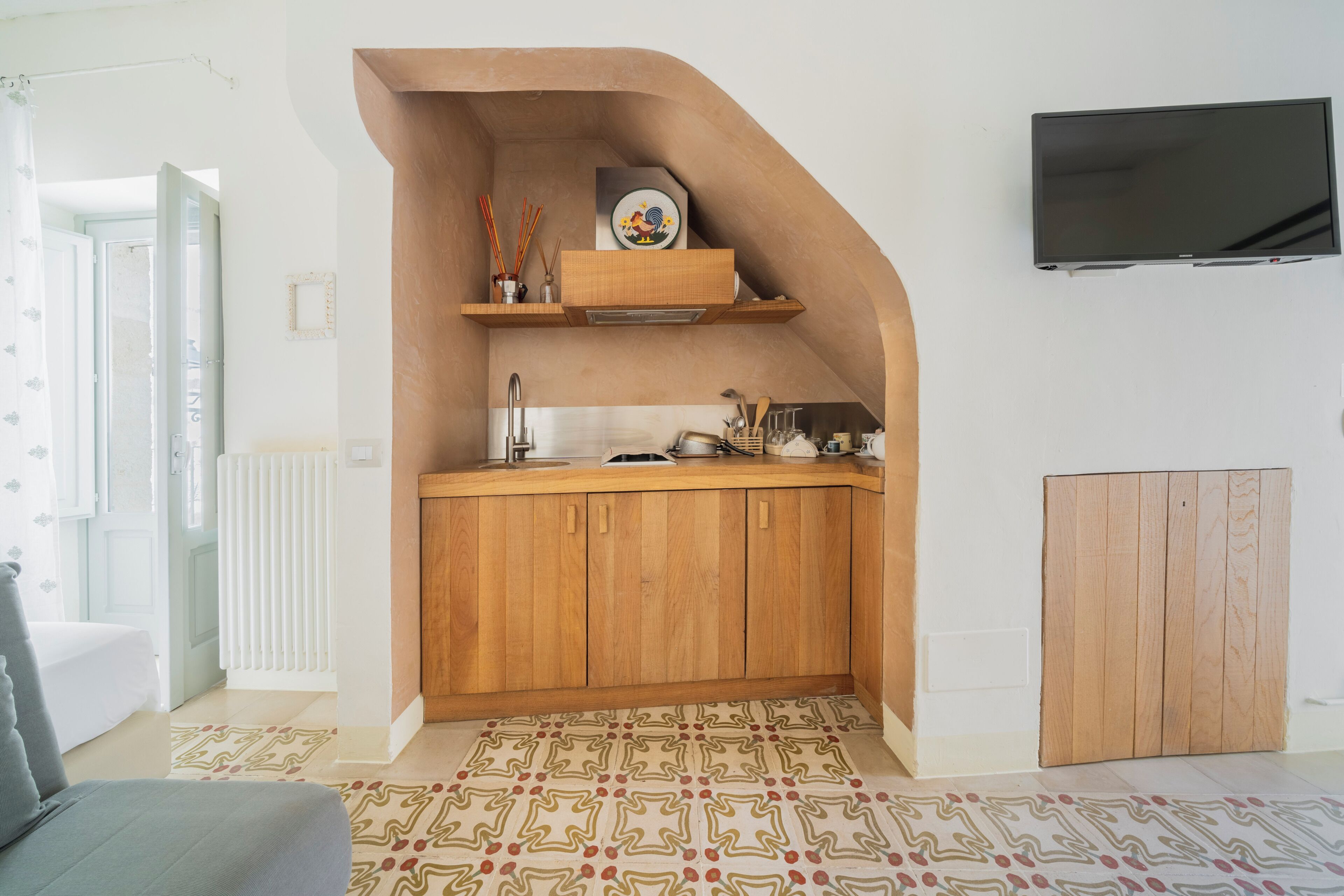A compact kitchen with wooden cabinets, a built-in stove, and a TV mounted on the wall.