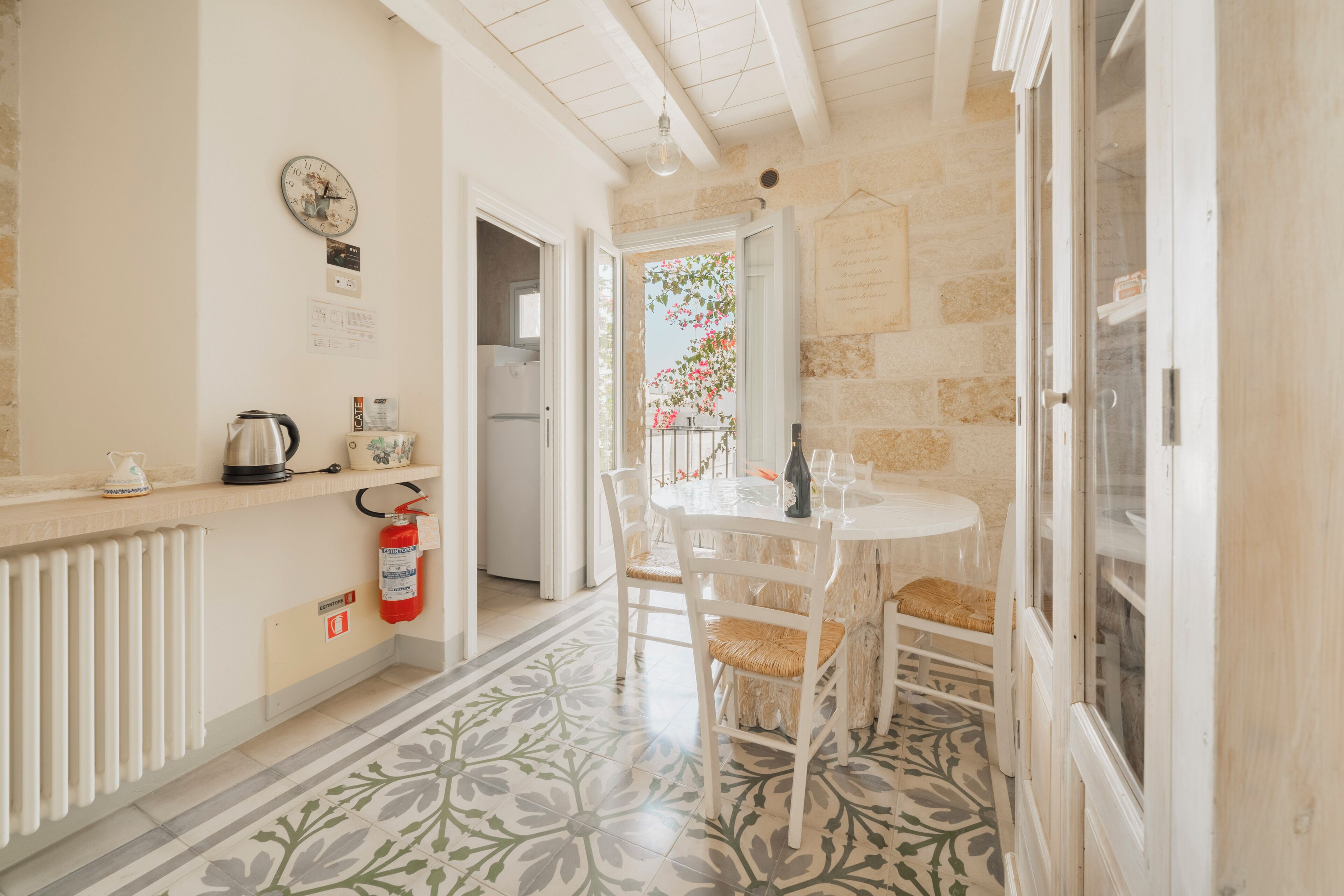 A kitchen with a white countertop, a clock, a fire extinguisher, and a view of the outside.