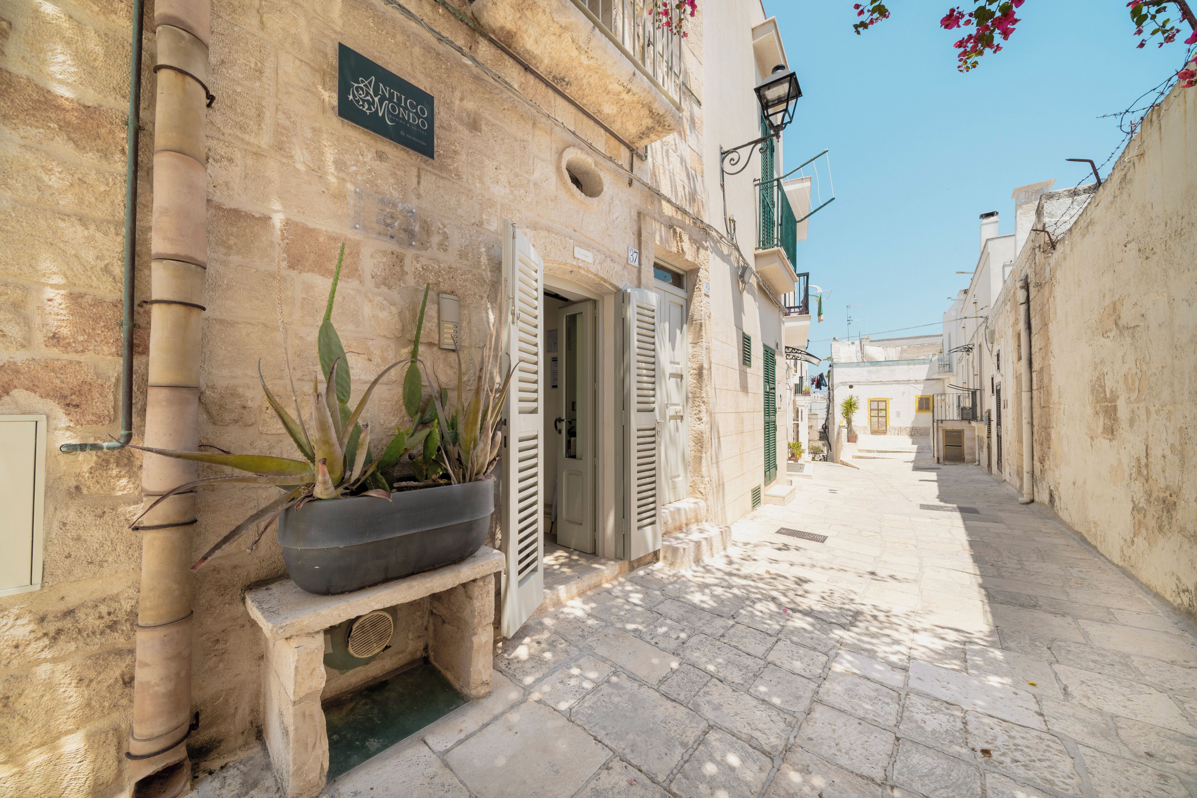 A narrow stone-paved street with buildings on either side, a bench with a potted plant, and a sign above a door.
