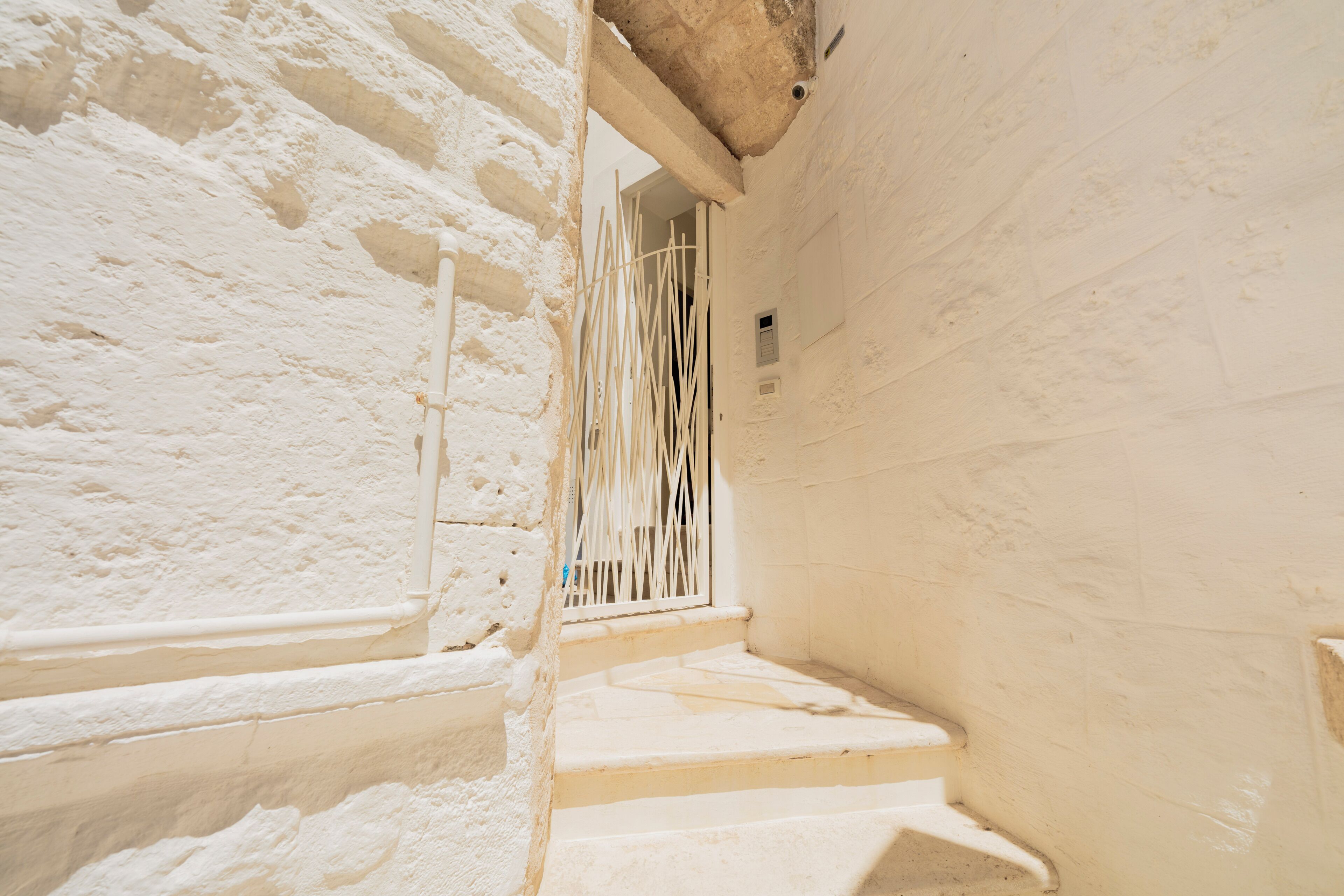 Una escalera estrecha que lleva a una puerta con un tragaluz con barrotes, rodeada de paredes blancas.