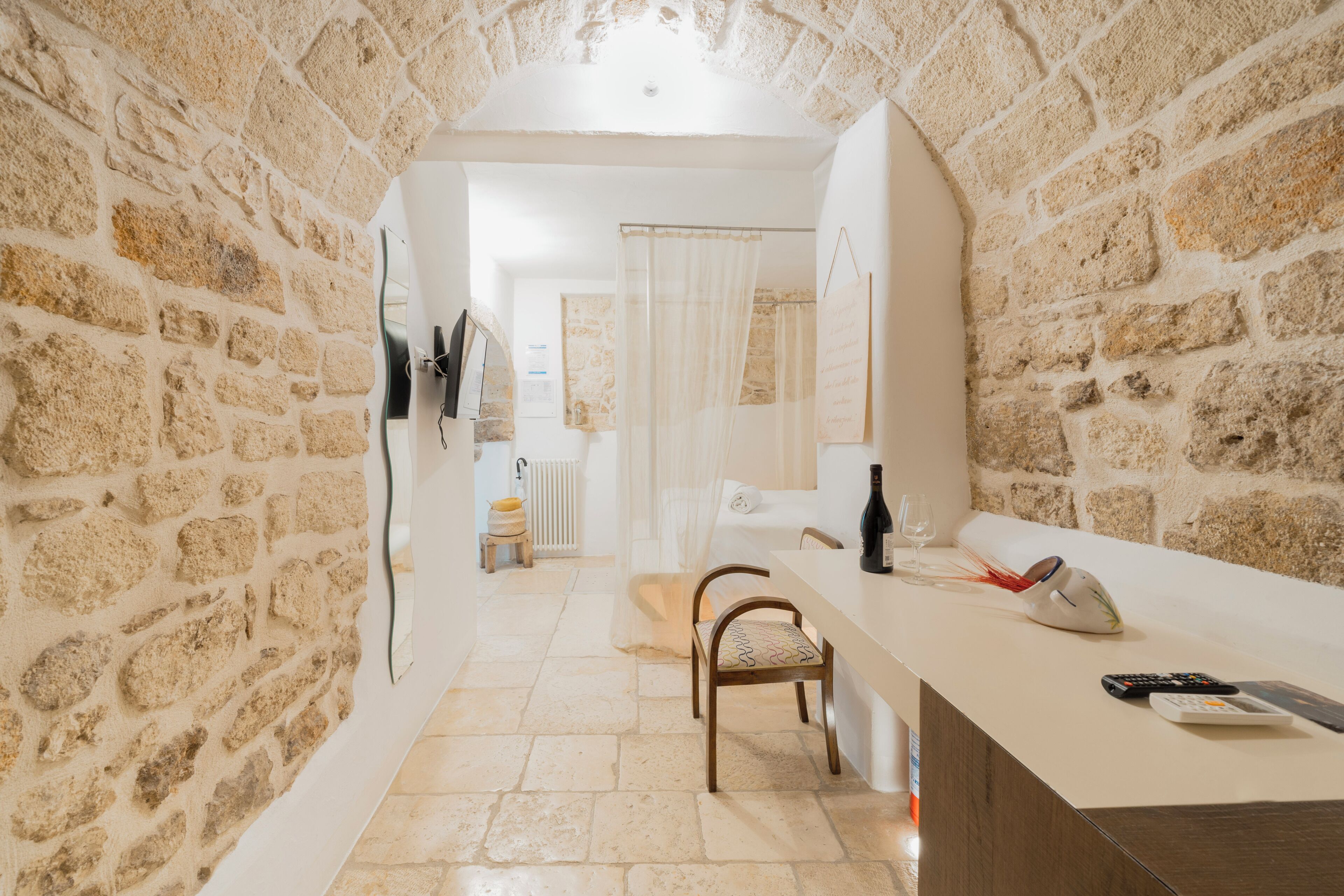 Una habitación con paredes de piedra, una silla de madera, una encimera con una botella y un control remoto.
