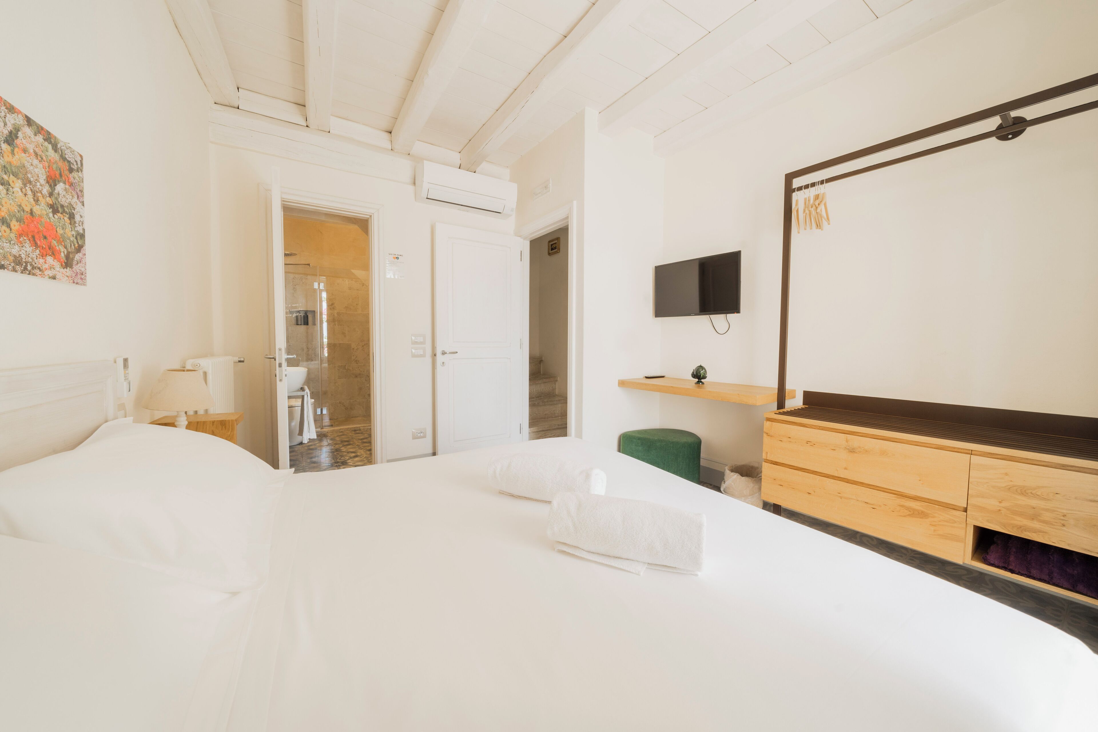 A hotel room with a bed, a TV, a wooden dresser, and a shower area.