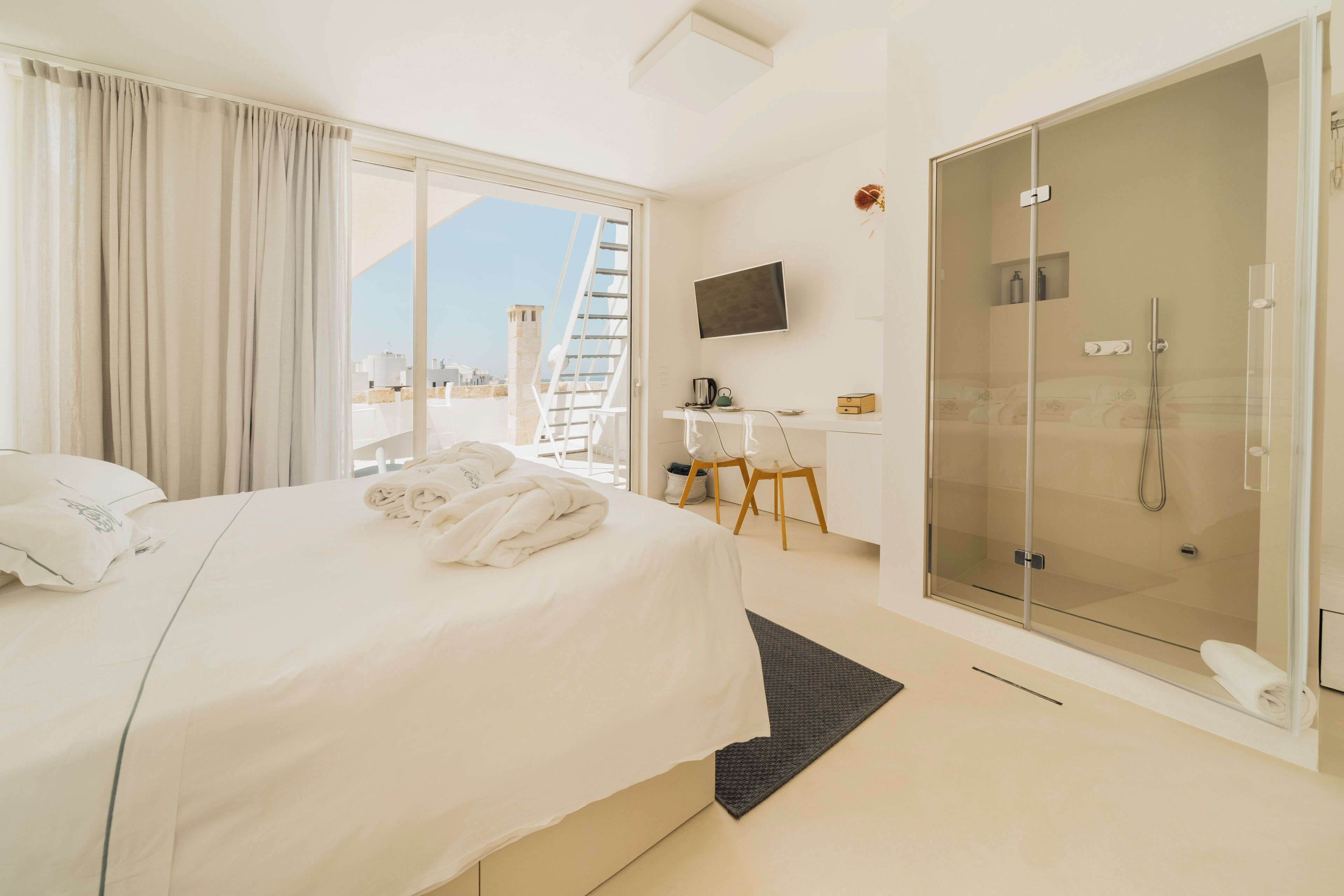A hotel room with a bed, a desk, a TV, and a glass shower.