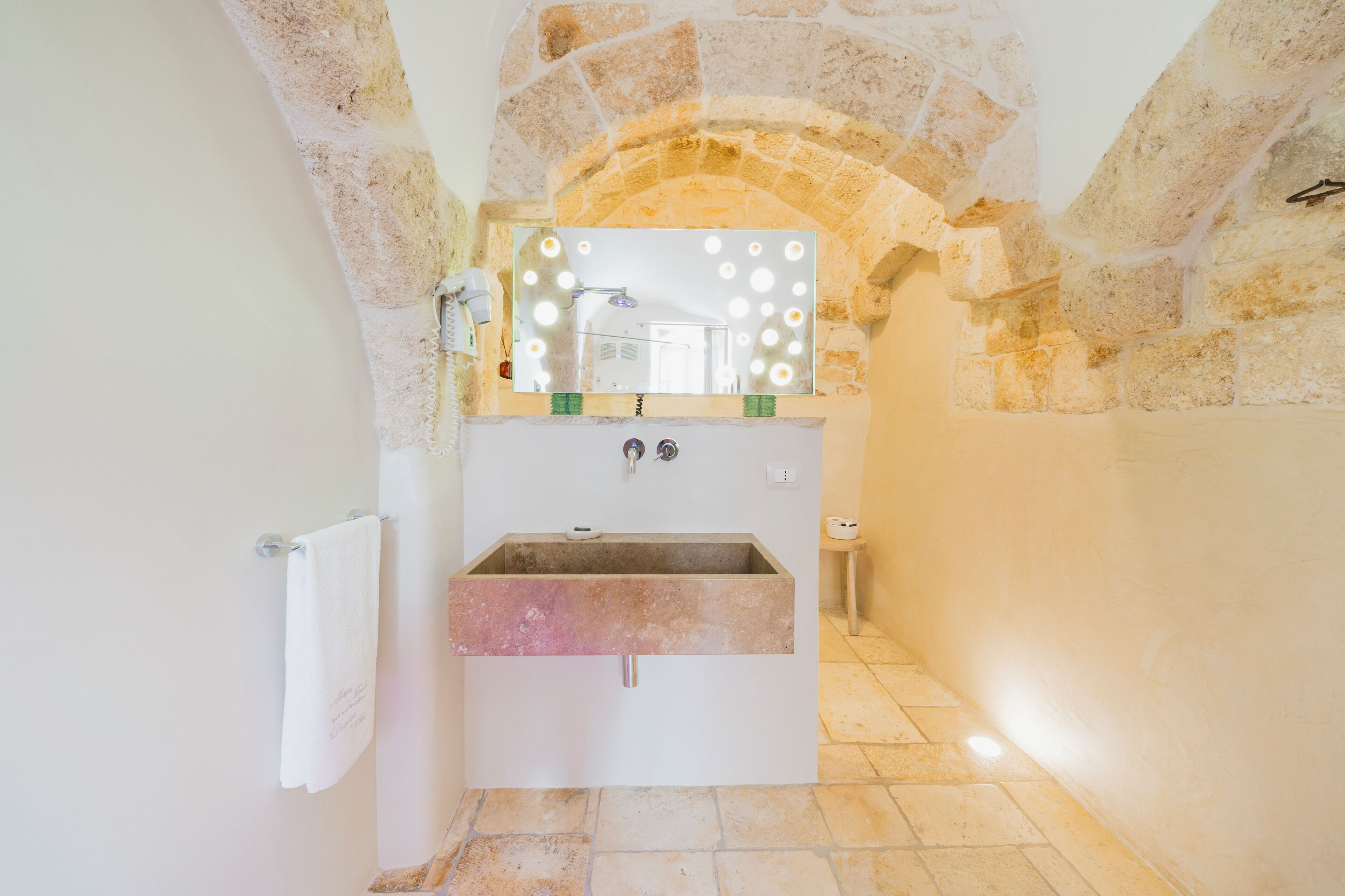 Un baño con un arco de piedra, un lavamanos con espejo y un perchero para toallas.