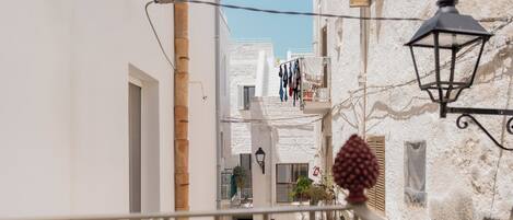 Una calle estrecha con edificios blancos, un balcón con ropa tendida y un farol.
