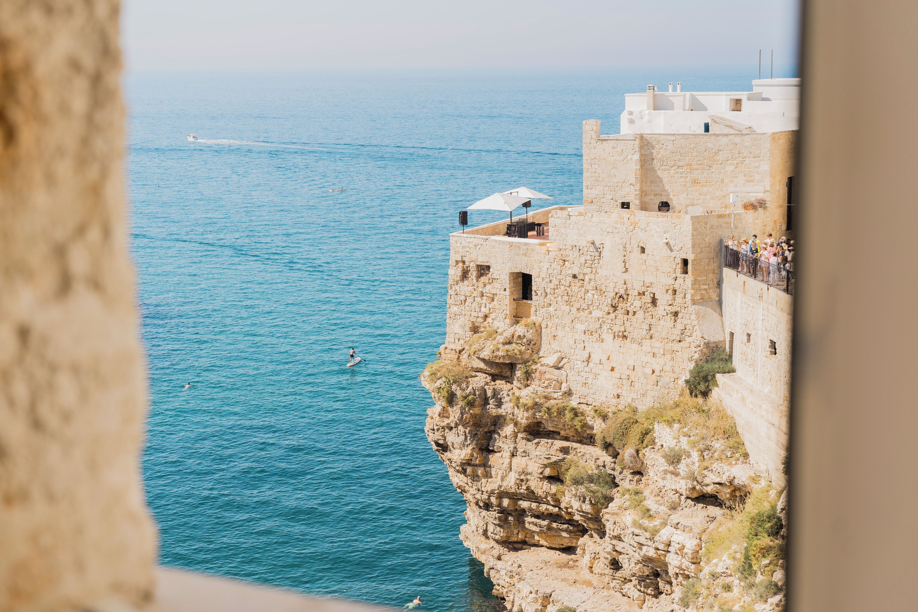 A coastal cliff with stone buildings, a view of the sea, and a person swimming.