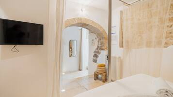 Una camera da letto con un letto, una televisione a parete, un arco in pietra e uno sgabello.