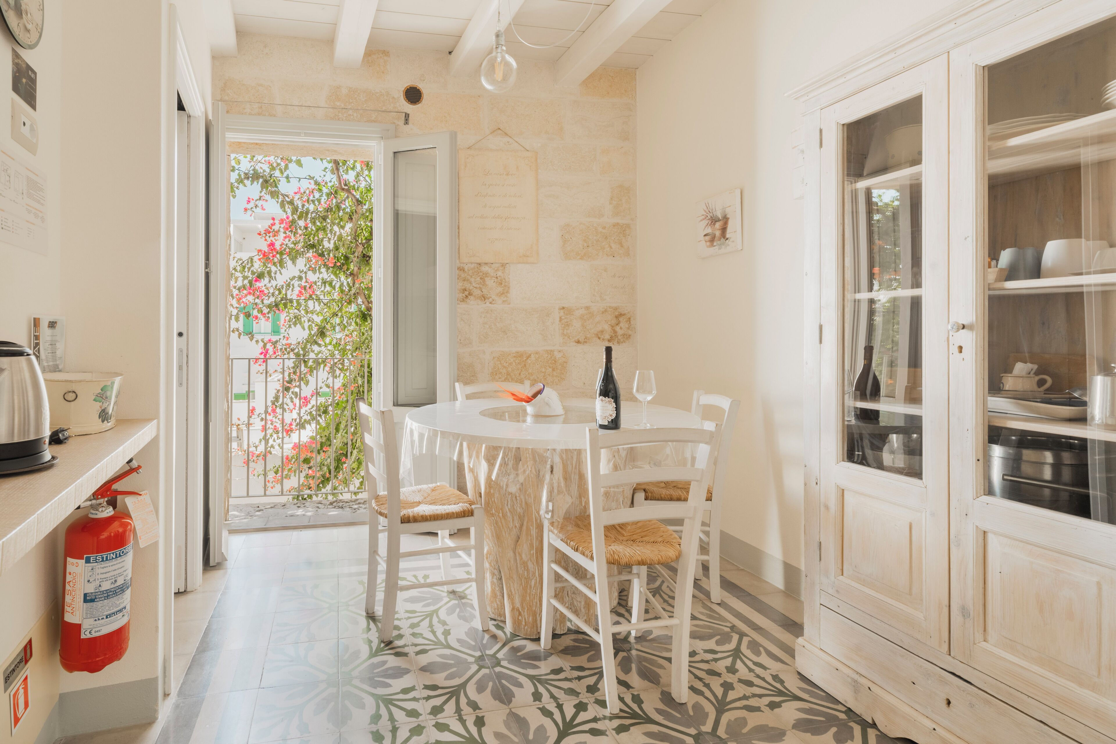A kitchen with a round table, chairs, a wine bottle, and a fire extinguisher.