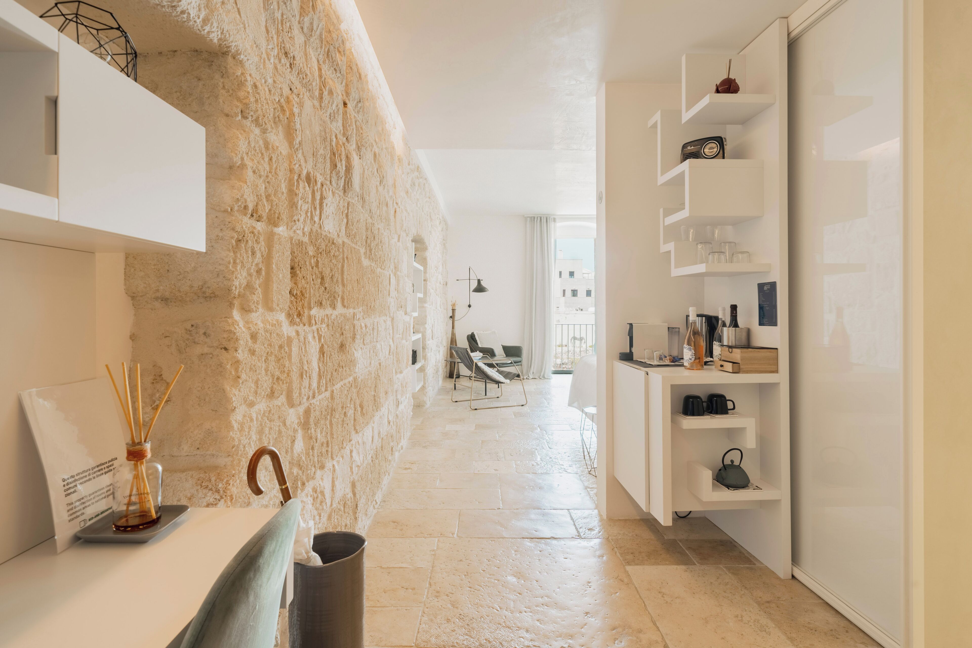 Un interior moderno con pared de piedra, mobiliario blanco y vistas al exterior.