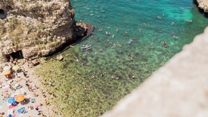 Una playa con aguas cristalinas, acantilados rocosos y gente nadando y tomando el sol.