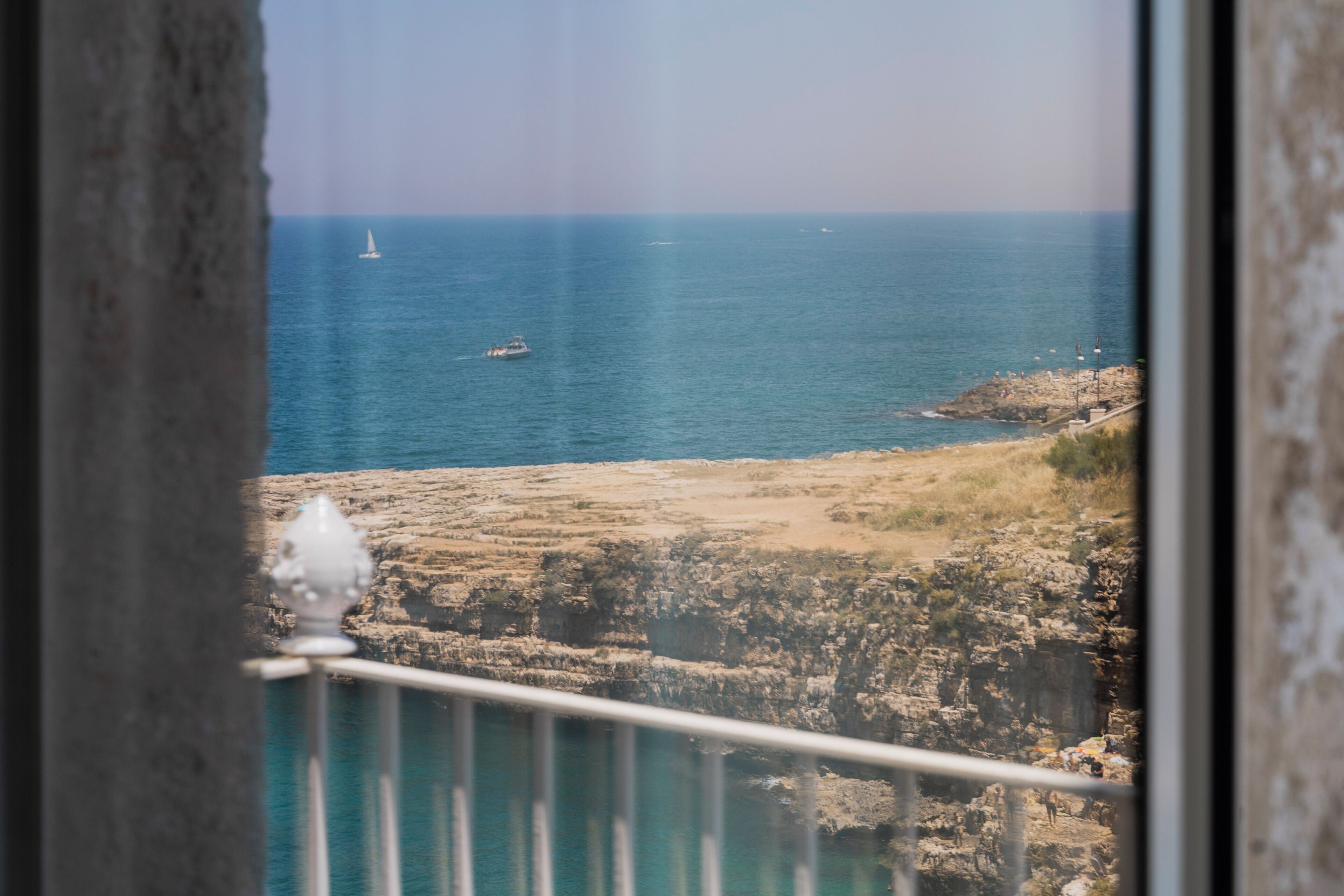 A coastal view with a rocky shoreline, a boat in the distance, and a railing in the foreground.